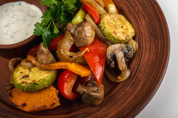 Delicious roasted vegetables on a rustic brown plate with creamy dipping sauce. Grilled zucchini, mushrooms, bell peppers, onions, and parsley garnish for a healthy meal