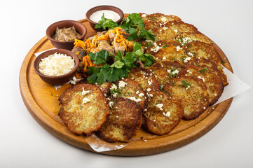 Traditional Belarusian or Ukrainian potato pancakes with fried meat, sauted vegetables, sour cream, cheese, mushroom sauce, and fresh herbs on a wooden platter