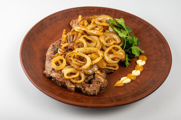 Grilled pork steak with golden fried onions served on a rustic clay plate. Traditional Eastern European dish with mustard, mayonnaise and fresh parsley garnish, on a light background