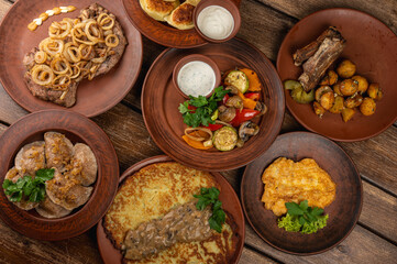 Traditional Eastern European cuisine served on rustic clay plates. Variety of homemade dishes including meat, potatoes, pancakes, dumplings, and grilled vegetables, on a wooden background