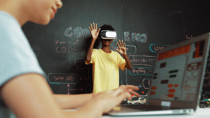 Closeup of school girl hand coding program while african student using VR interact with metaworld. Smart boy wearing virtual reality glasses and playing video games at innovative class. Edification.
