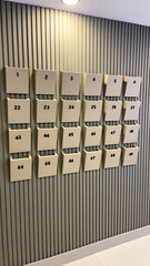 Modern Beige Mailboxes With Black Numbers Mounted On Vertical Slatted Wall Indoors, Concept Of Organized Living, Mail Management, And Residential Interior Design In Apartment Buildings