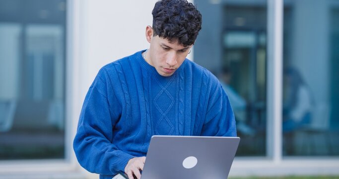 Focused student working on laptop outside university building