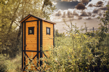 A small wooden toilet, surrounded by trees