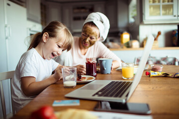 Single mother and daughter having breakfast together in the morning while using a laptop in the kitchen