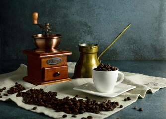Coffee grinder, coffee beans and espresso cup laid on table cover.