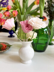 Pink and white lisianthus flowers in small white vase among colorful tulip arrangements. Home decoration and floral composition
