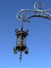 An ornate vintage lantern with intricate metal scrollwork, suspended from a decorative wrought iron...