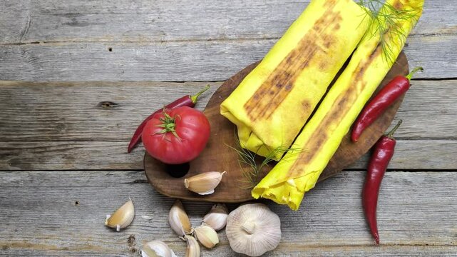 Cheese shawarma lies on a cutting board next to red pepper and heads of garlic
