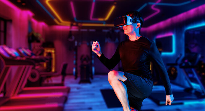 Asian man with VR glasses playing fitness while exercising at fitness. Male model using augmented reality and artificial intelligence to plan exercise plan. Technology innovation concept. Ingenuity.