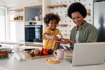 Joyful African American Mother Teaching Young Son Cooking Skills While Preparing Fresh Ingredients...