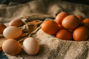 Fresh farm eggs in various shades of brown and cream on burlap and wooden boards. Rustic kitchen setting with wooden spoons, jute twine, and natural light