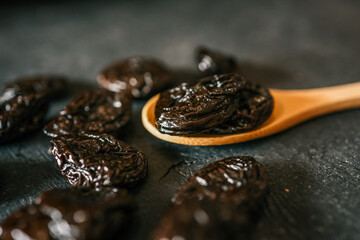 Dried prunes on a wooden spoon and dark textured background. Healthy organic snack rich in fiber and antioxidants, perfect for digestion and natural sweetness in diet