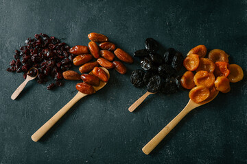 Four types of dried fruits-cranberries, dates, prunes, and apricots-arranged in rows on a dark...