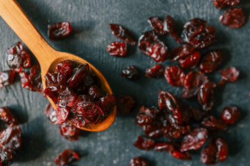 Top view of dried cranberries on a dark textured surface with a wooden spoon. Glossy red berries...