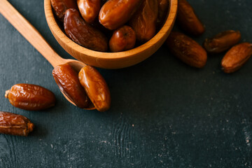 Close-up of sweet dried dates in a wooden bowl and spoon on a dark background. Natural snack rich in fiber and energy, perfect for healthy eating and Ramadan
