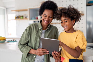 Joyful African American Mother And Daughter Sharing Digital Tablet Moment In Contemporary Home Kitchen Setting