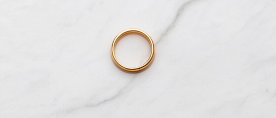 Close-up of a gold ring on a white marble surface. the ring appears to be made of gold and has a smooth, polished finish. it is in the shape of an oval with a thin band that curves around the edges.