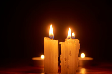 Burning white wax candles glowing softly, casting warm light against dark shadows, symbolizing...