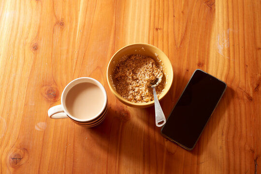 Wooden table hosting nutritious morning essentials: steaming oatmeal, freshly brewed coffee, smartphone signaling contemporary breakfast routine