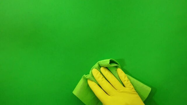 Wiping the window pane with a bright green cloth. Cleaning the surface with a dark green cloth. A hand wearing a yellow rubber glove wipes the surface. Chroma key background. Housekeeping and neat cle