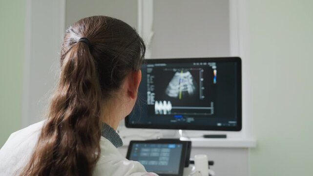 Female radiographer attentively observes waveforms on examination machine screen in clinical room, monitoring diagnostic data in real time to evaluate internal body activity during scan session