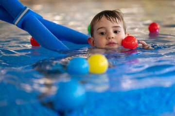 Child swimming with colorful balls and floatation device in pool