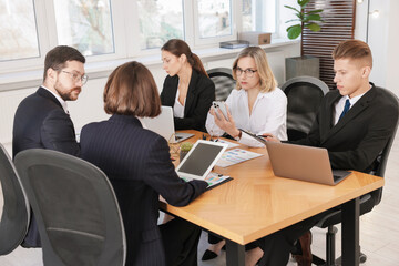 Coworkers with different devices working together at wooden table in office
