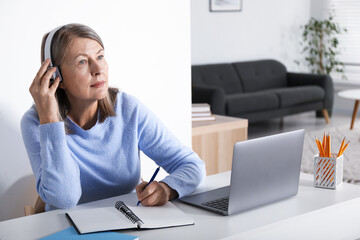 Woman learning online using laptop and taking notes at table indoors. Self-study