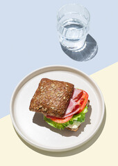 Toast sandwich made of grain bread with prosciutto, tomatoes, lettuce and sauce on blue yellow background