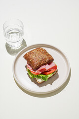 Toast sandwich made of grain bread with prosciutto, tomatoes, lettuce and sauce on light background