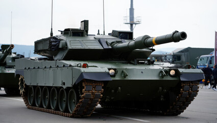A military tank is prominently displayed on a parade route during a military exhibition in spring. The tank showcases its robust design and advanced features for attendees to observe