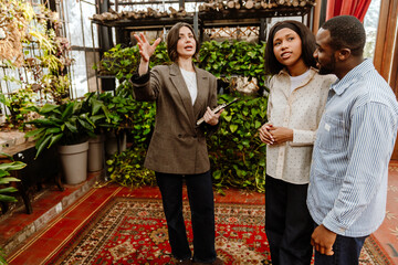 A man and a woman stand and listen to a female organizer who stands next to them and holds a...