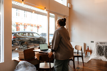 The female owner is standing and leaning on a chair while looking out the window, preparing for the opening of the cafe