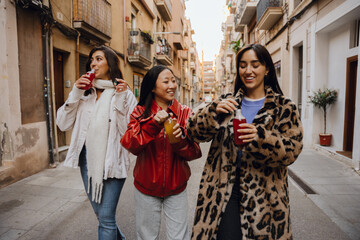Group of three women walking and smiling while talking and holding bottles, outdoors, at a girls' party
