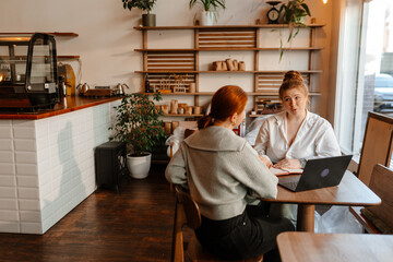 Female owner sitting at a table and talking to a female employee sitting across from her, preparing...
