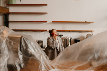The woman owner is standing and smiling while talking on the phone and looking up, preparing to...