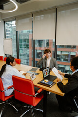 Obraz premium Two female employees sitting at a table and holding papers while looking at a male intern sitting next to them and smiling, in the office, during an internship