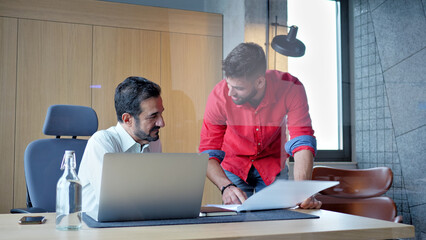 In a modern office, two men collaborate on a laptop, symbolizing teamwork and innovation. A side...