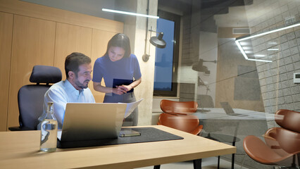 A man and woman in a modern office setting collaborate on a laptop, symbolizing teamwork and productivity.