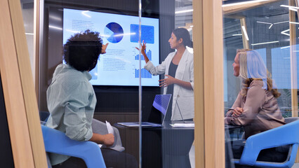 In a modern office, a woman presents data on a large screen to two colleagues, symbolizing effective teamwork and collaboration.
