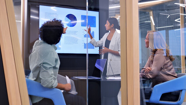 In a modern office, a woman presents data on a large screen to two colleagues, symbolizing effective teamwork and collaboration.