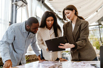 A light-skinned female wedding planner shows a black planchette with info to a Black young couple...