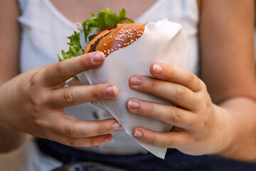 Closeup of young womans hand grabbing  juicy double cheeseburger with sesame seed bun, fresh...