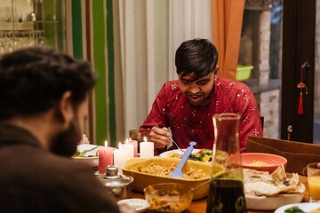 An Indian young man enjoying a joyful dinner with family, seated at a well-decorated table with...