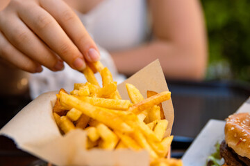 Closeup of young womans hand grabbing a crispy golden fries. Enjoying potato chips with a juicy...