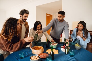 A multinational group of young people celebrating a birthday party, gathering around a table with...