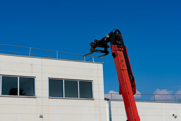 A red forklift stretches its arm towards the top of a building
