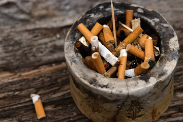 Closeup of an ashtray filled with numerous cigarette butts on a wooden surface, symbolizing smoking habits and litter, smoking harm, urban pollution, unhealthy lifestyle, littering.