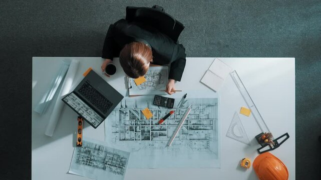 Top view of architect engineer drink coffee and draw blueprint at meeting table with equipment and safety helmet scatter around. Aerial view of project manager looking at project plan. Alimentation.